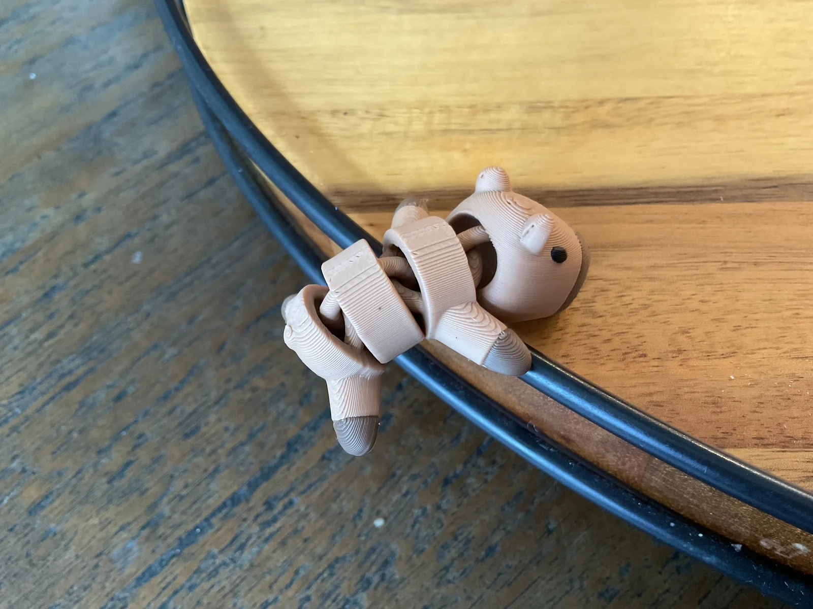 Tan articulated Baby Capybara curled playfully over the edge of a table